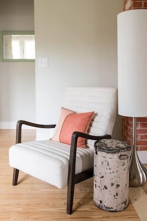A chair with a cushion, a lamp, and a textured container on a wooden floor.