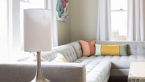 Een woonkamer met een bank, een lamp, een schilderij en een raam met gordijnen.