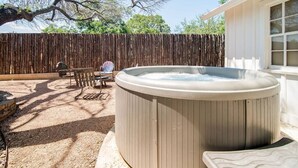 Een hottub in een achtertuin met een houten schutting, een patio tafel en een stoel.