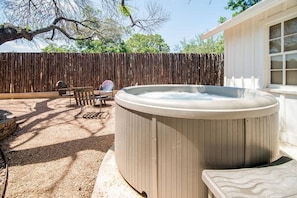 Un jacuzzi en un patio trasero con cerco de madera, una mesa de patio y una silla.