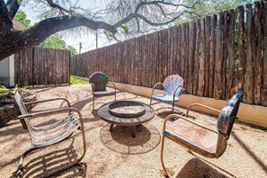 A backyard with a wooden fence, a fire pit, and two metal chairs.