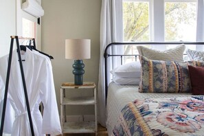 A bedroom with a bed, a lamp, a clothing rack, and a window with a view of trees. - Pet-Friendly Craftsman Home in Fredericksburg (Fredericksburg)