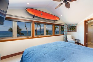Ein Schlafzimmer mit einem großen Bett, einem Deckenventilator und einem Wandregal mit einem Surfbrett.