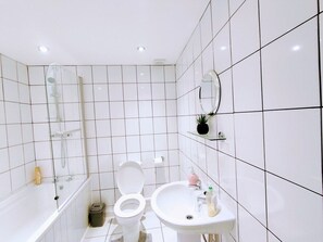Uma casa de banho moderna com azulejos brancos, cabine de duche em vidro, sanita, lavatório e espelho.