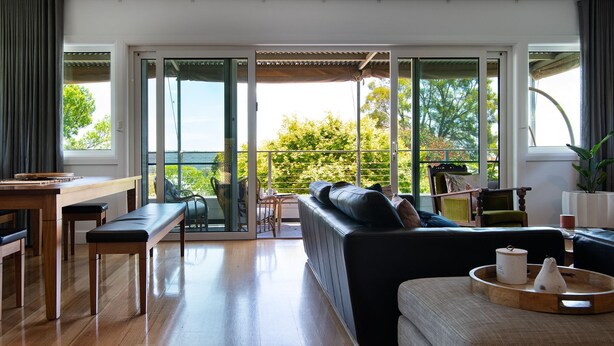 Ein geräumiger Wohnbereich mit einer großen Glasschiebetür, die auf einen Balkon führt, einem Holzessttisch, einem Sofa und einem Couchtisch mit Tablett.