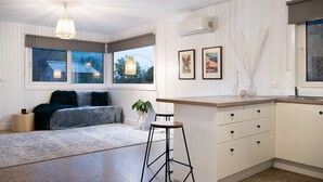 Eine moderne Küche mit Barhocker, Esstisch und Sofa. An der Wand befinden sich Bilderrahmen und ein Fenster mit Außenblick.