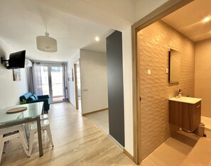 Un salon moderne avec une table à manger en verre, un canapé et un téléviseur à écran plat fixé au mur.
