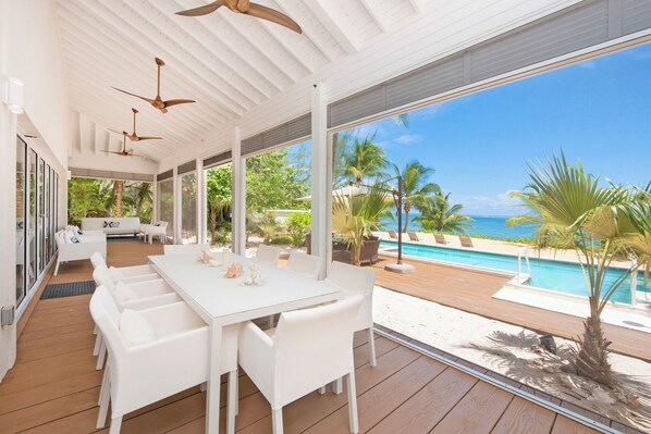 A covered outdoor dining area with a pool and ocean view.