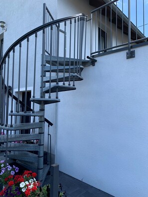 Un escalier en colimaçon avec des rampes en métal, adossé à un mur blanc, et menant à l’étage supérieur.