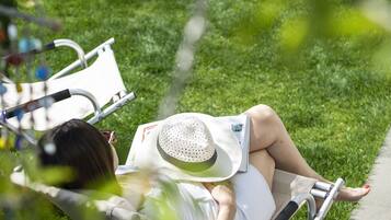 A person lying on a lawn chair in a grassy area with a table and chairs in the background.
