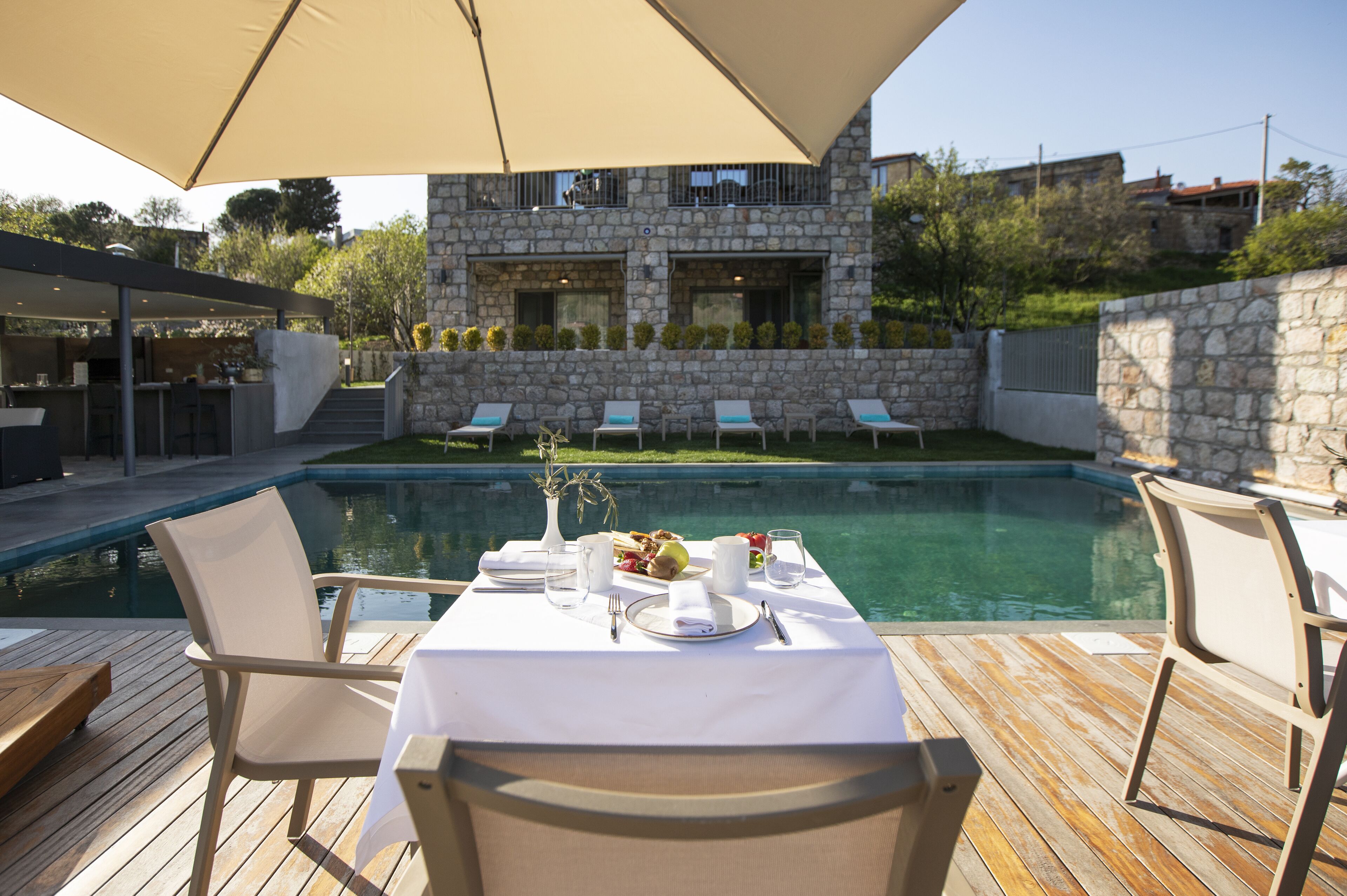 Ein Essbereich am Pool mit Tisch für zwei Personen, mit Blick auf einen Swimmingpool und ein Steinhaus.