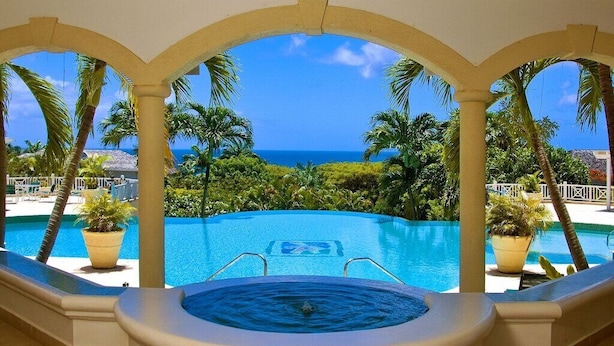 A hot tub with a pool view, surrounded by palm trees and a clear blue sky.