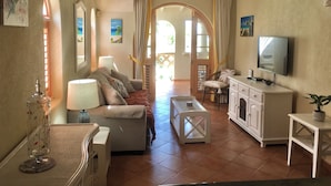 A living room with a sofa, coffee table, TV, and a fireplace. There is a window with curtains and a door leading outside.