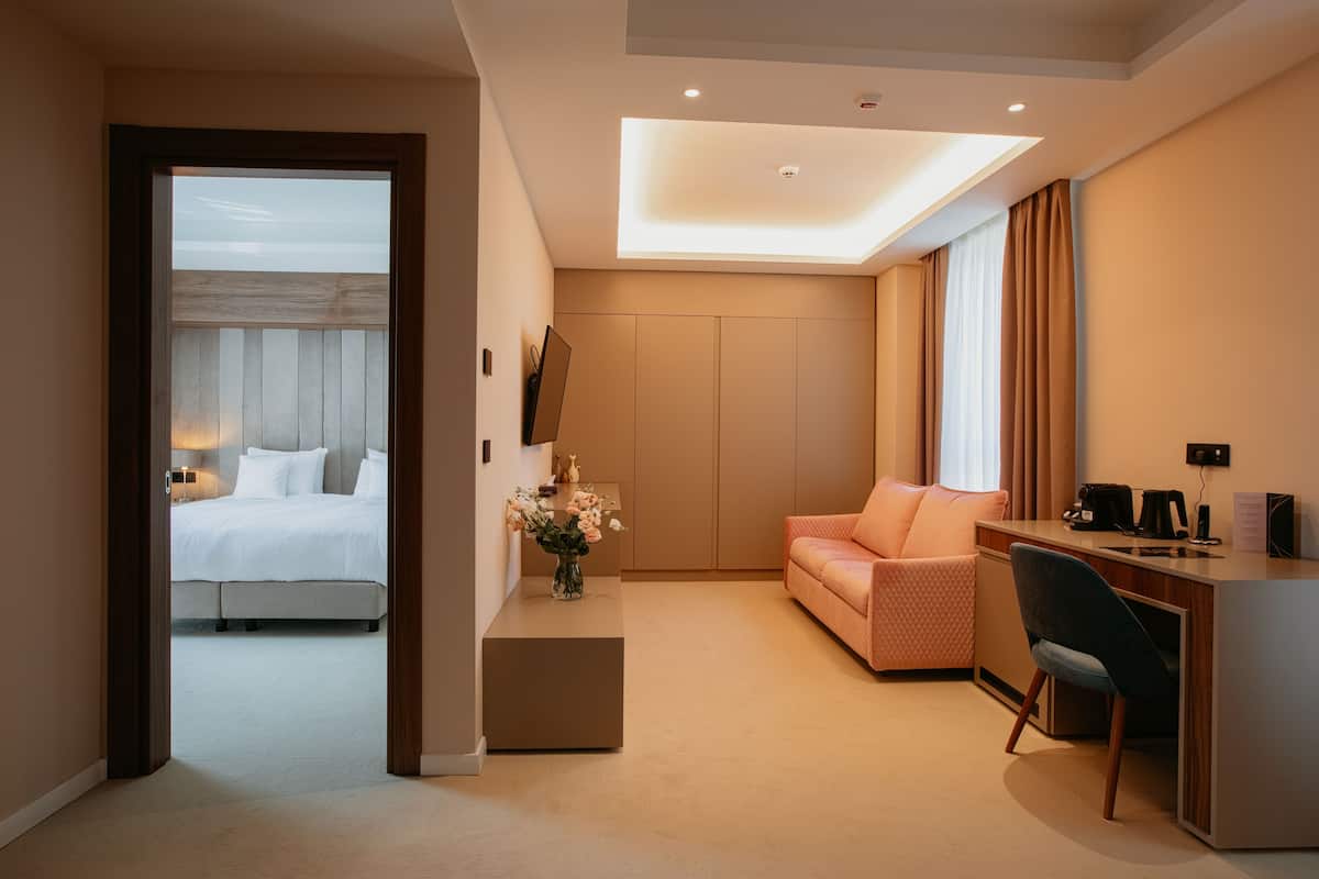A modern hotel room with a bed, a desk, a sofa, and a small table with a vase of flowers.