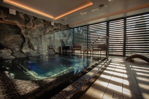 A modern indoor pool with a stone wall and a view of the outdoors through large windows. - Stein Collection (Dumbravita)