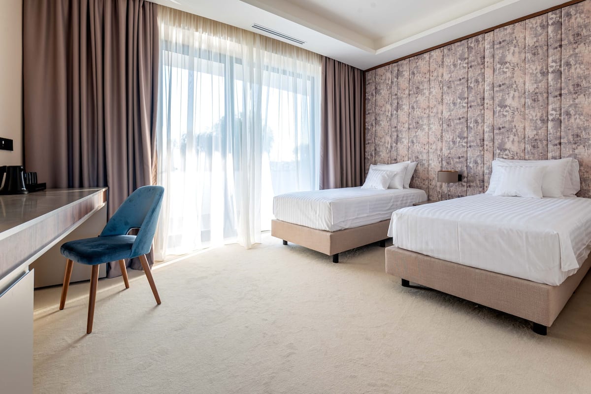 A hotel room with two beds, a desk, a chair, and a large window with curtains.