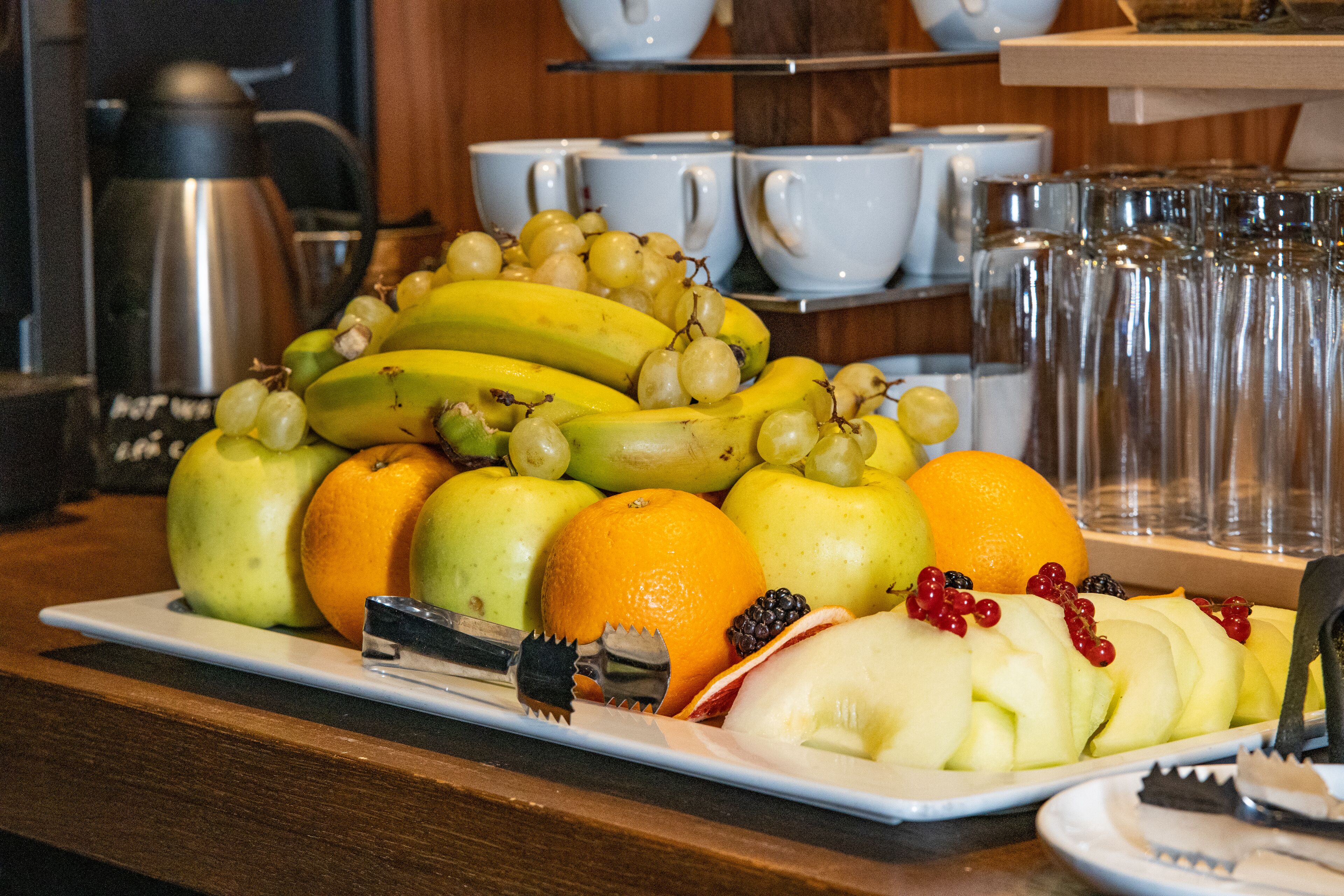 Una bandeja de frutas con plátanos, manzanas, naranjas y uvas sobre un plato blanco.