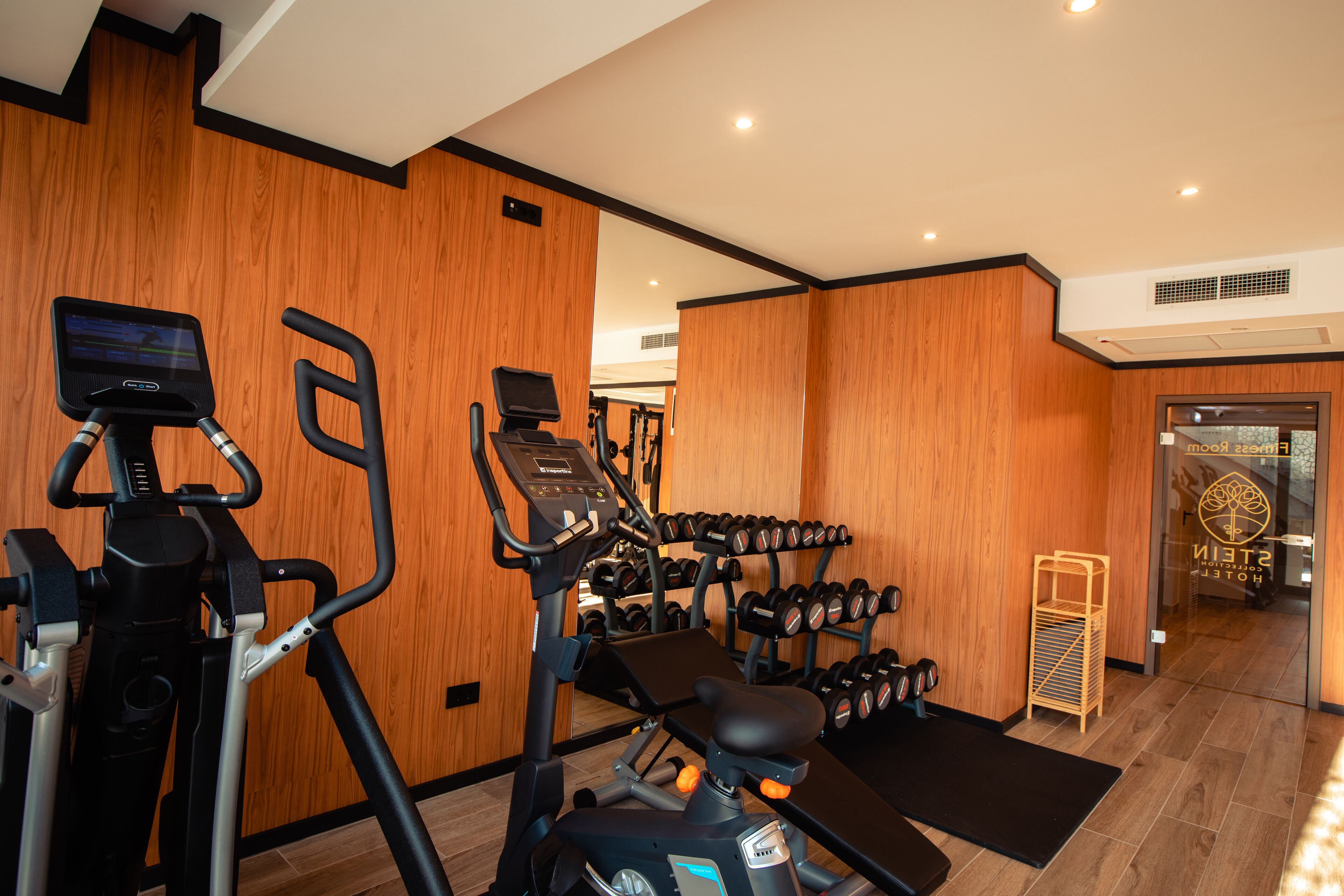Une salle de sport équipée de matériel d’exercice, notamment des tapis de course et des haltères, et dont les murs sont recouverts de lambris.