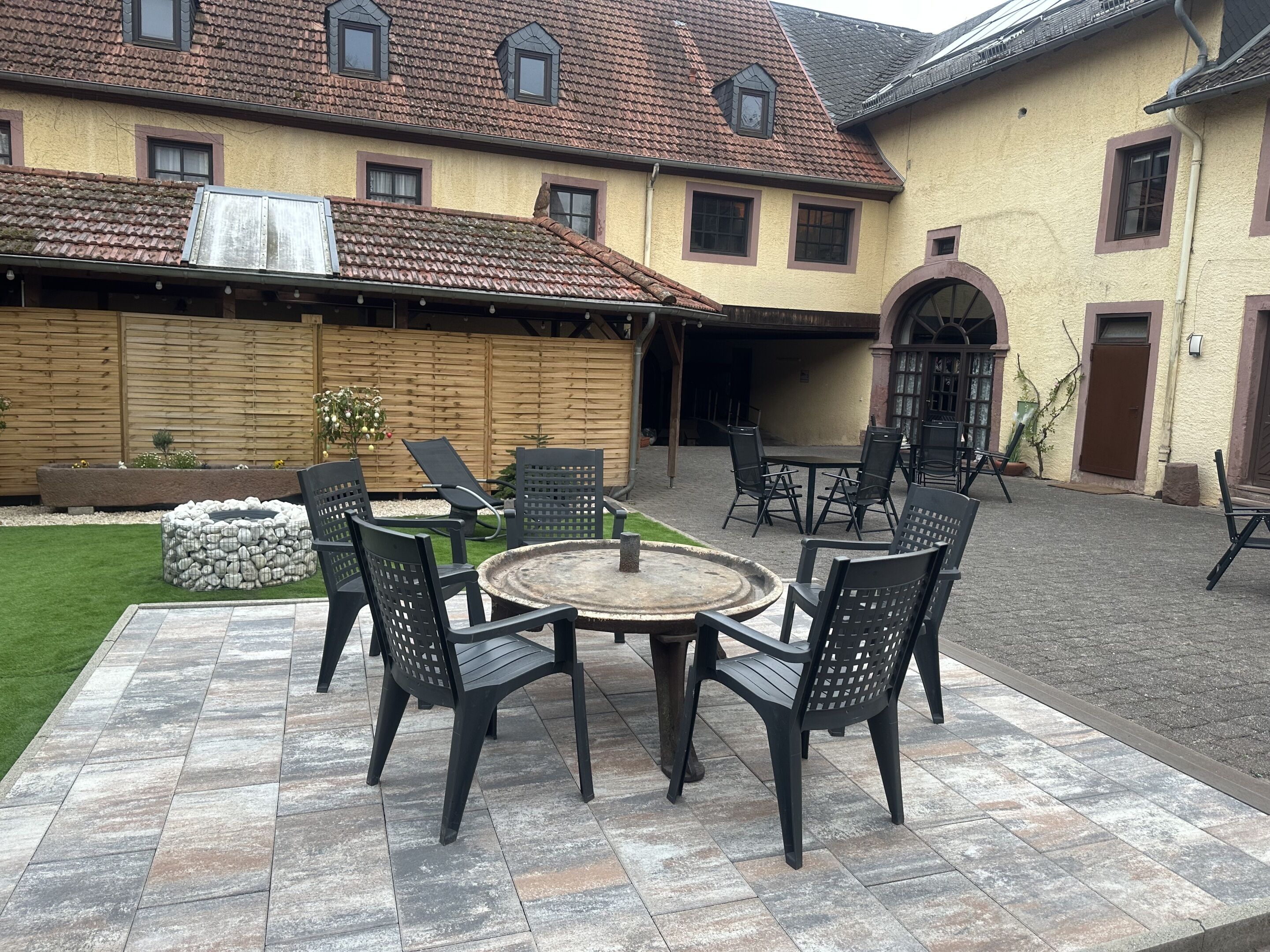 Eine Terrasse im Freien mit einem runden Tisch und Stühlen, einer Feuerstelle und einem Holzzaun.