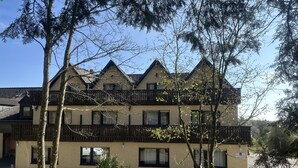 Un edificio de varios pisos con estilo arquitectónico tradicional, que cuenta con balcones y un estacionamiento al frente.