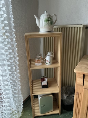 A stylish shelf unit against a striped wall, featuring a teapot, pitcher, and decorative container.