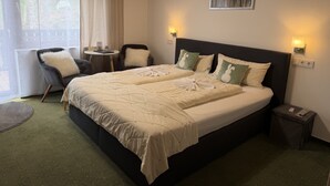 Habitación de hotel con una cama grande, dos sillones, una mesita y un cuadro en la pared, con vistas al exterior.