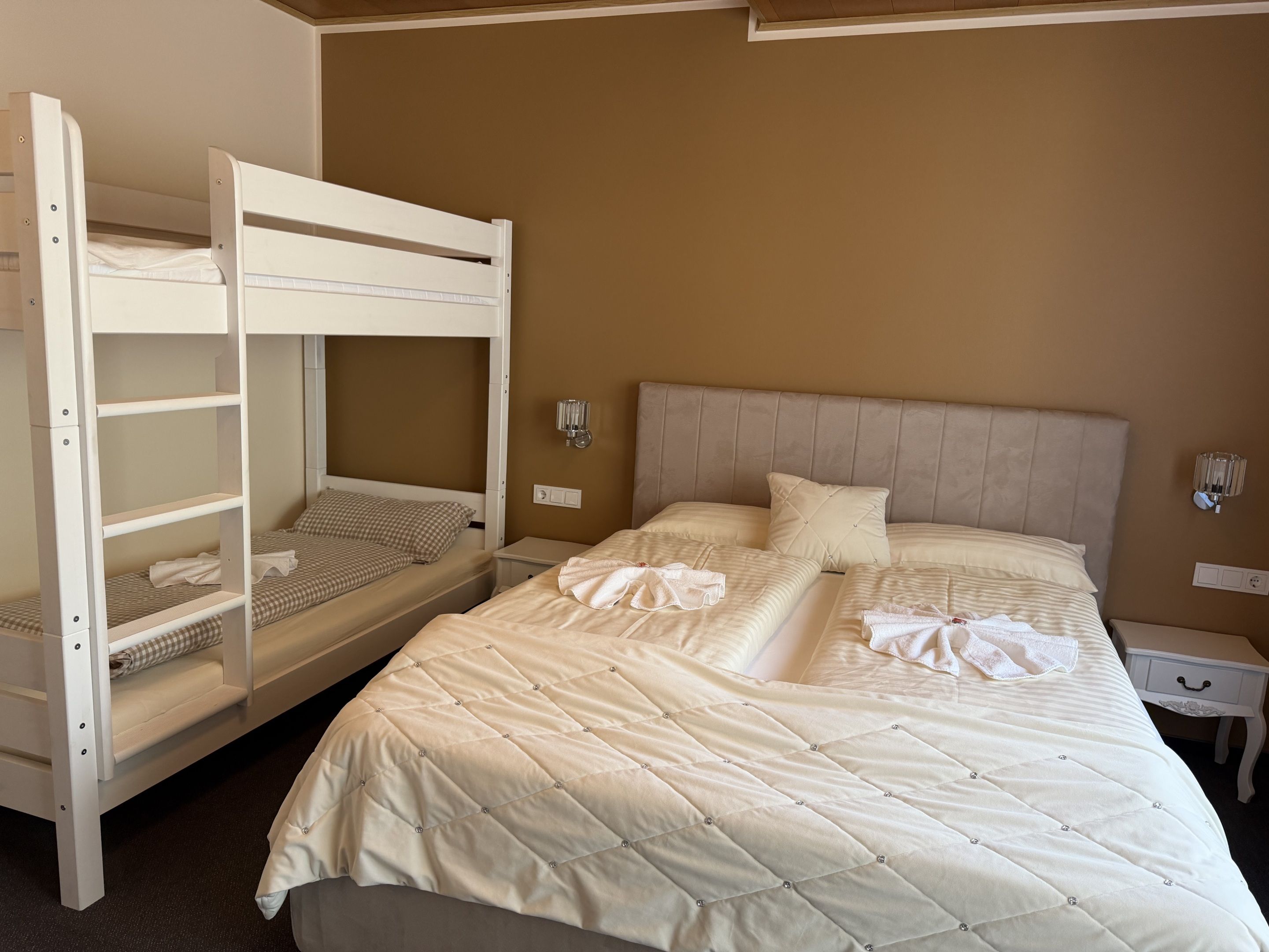 A hotel room with a bunk bed, a single bed, and a nightstand with a lamp.