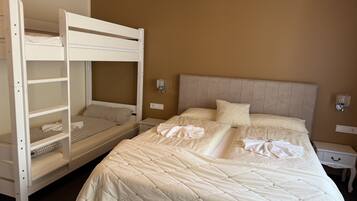A hotel room with a bunk bed, a single bed, and a nightstand with a lamp.