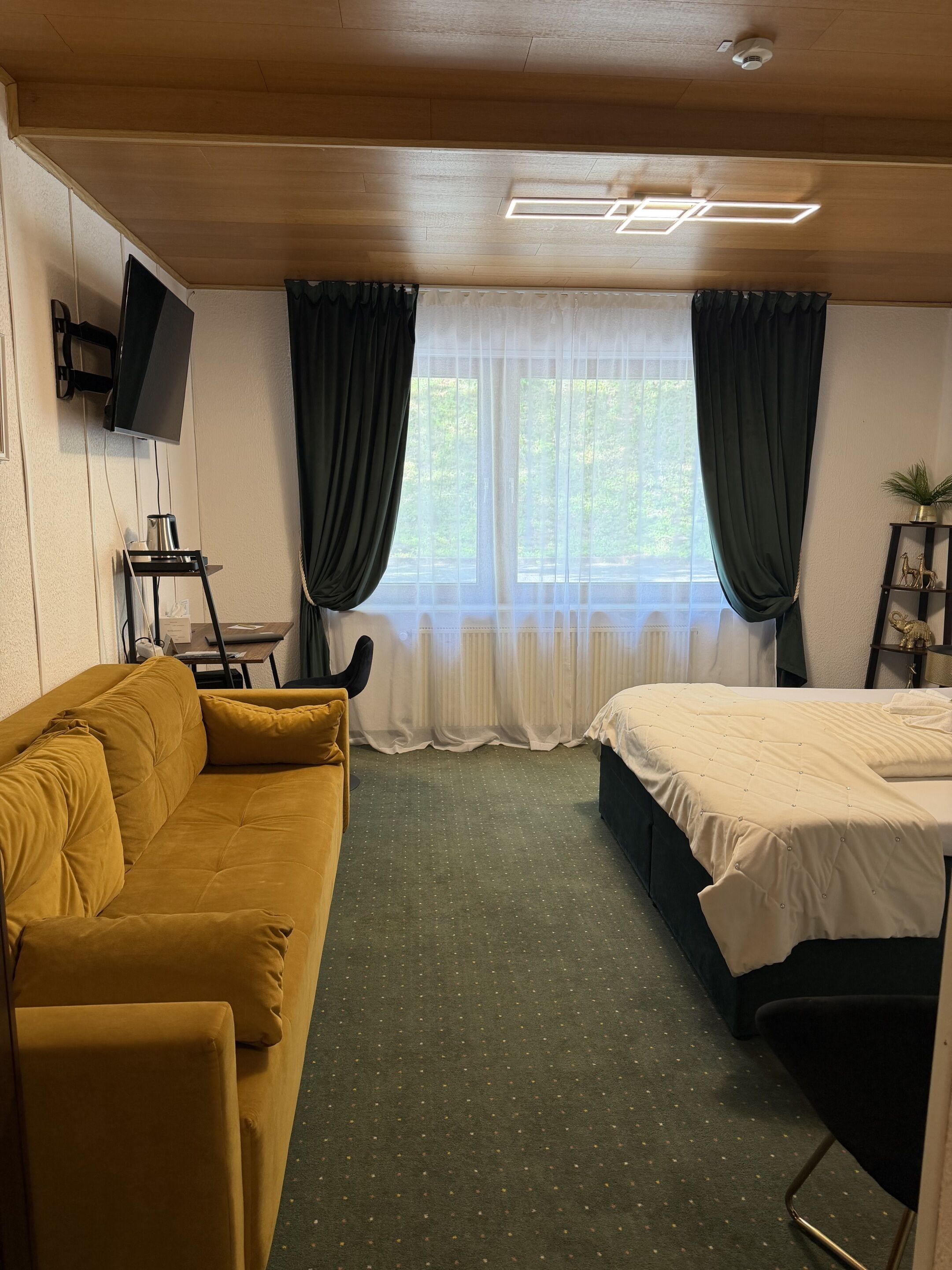 A room with a sofa, a bed, a TV mounted on the wall, and a window with curtains.
