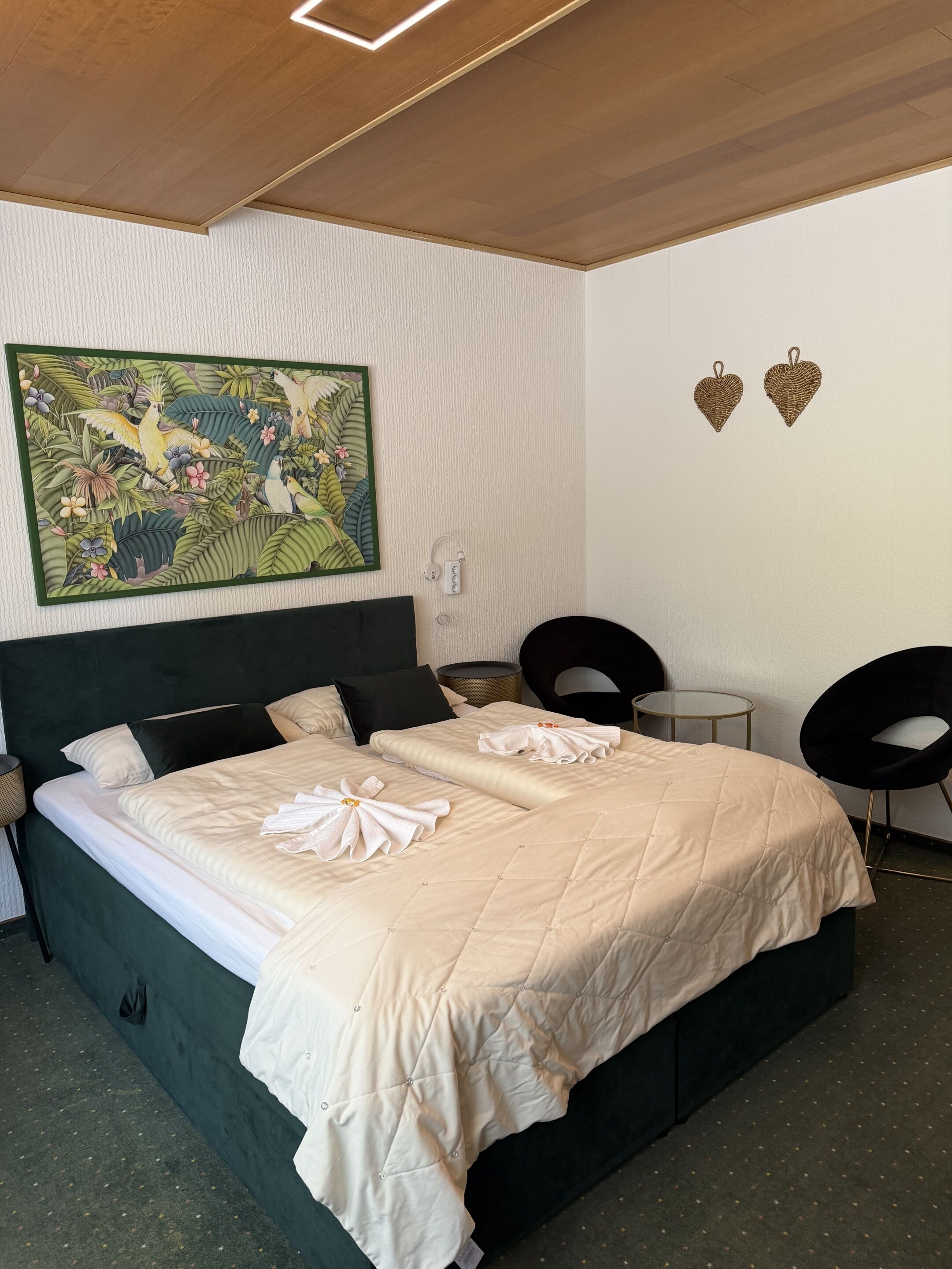 Una habitación de hotel con una cama grande, un cuadro en la pared, dos adornos con forma de corazón y una mesita.