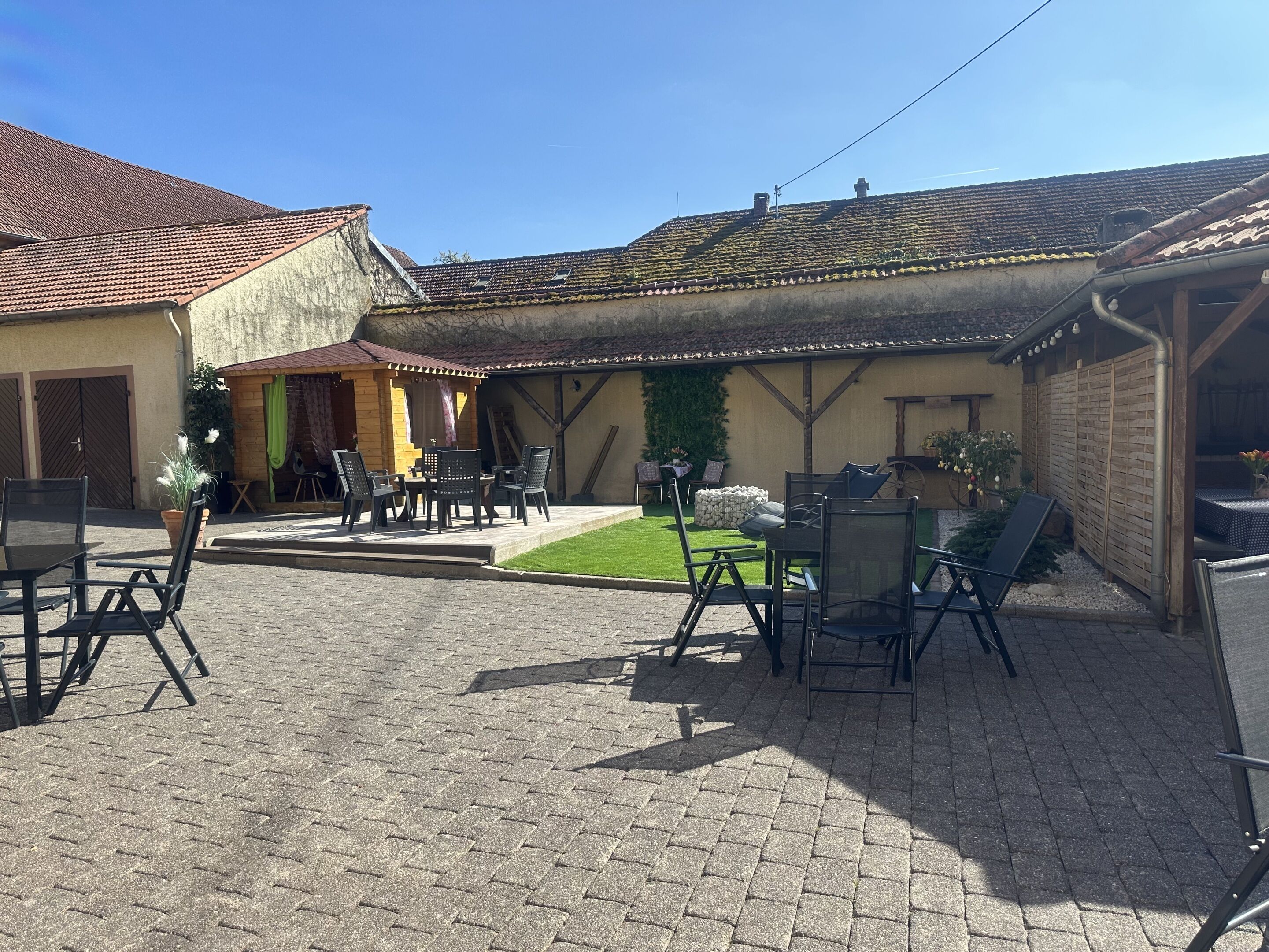 Une cour avec des sièges extérieurs, un petit jardin et un bâtiment doté d’un toit en tuiles.
