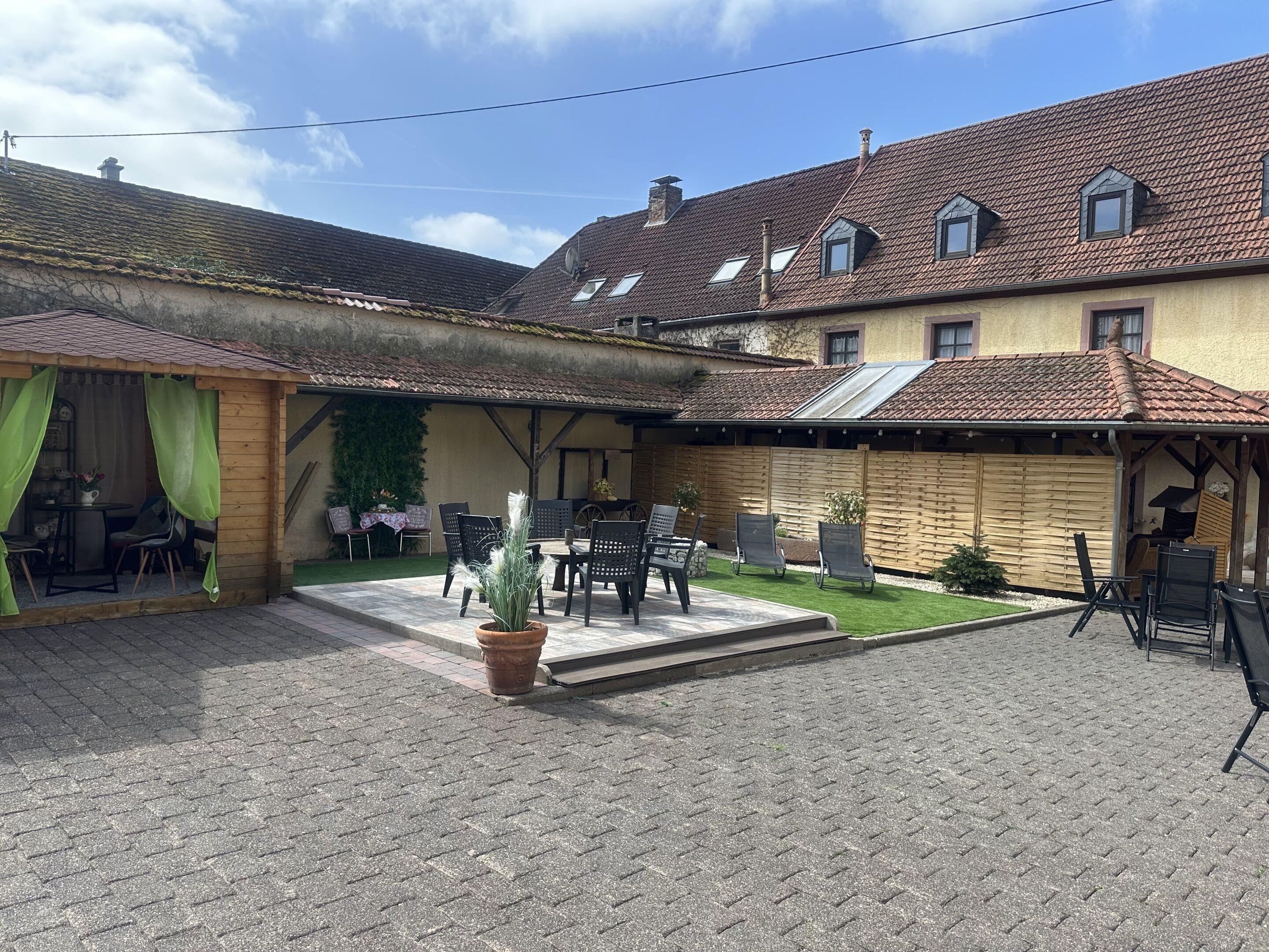 Ein Innenhof mit Außenbestuhlung, einem Blumentopf und einem Gebäude mit Ziegeldach und Holzbalken.