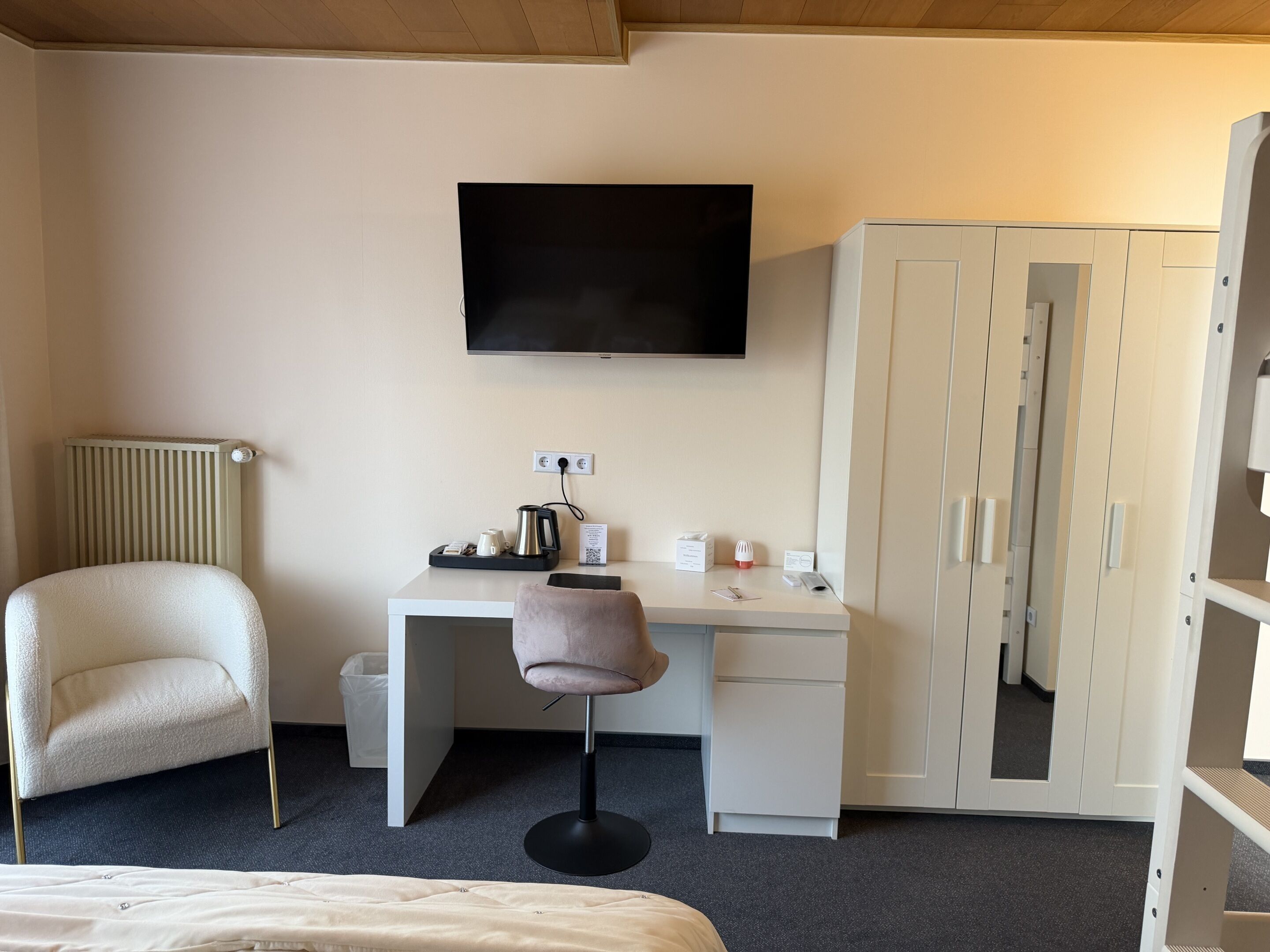 Una habitación de hotel con cama, escritorio con silla, televisión, armario y radiador.