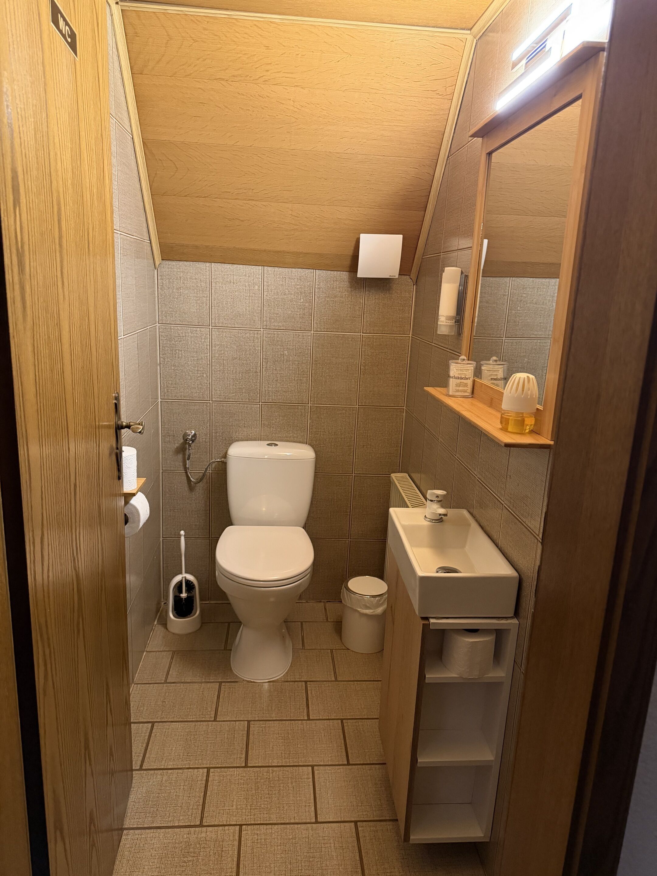 A compact bathroom with a toilet, sink, and storage shelves.