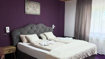 A bedroom with a bed, purple walls, a ceiling light fixture, and a window with curtains.