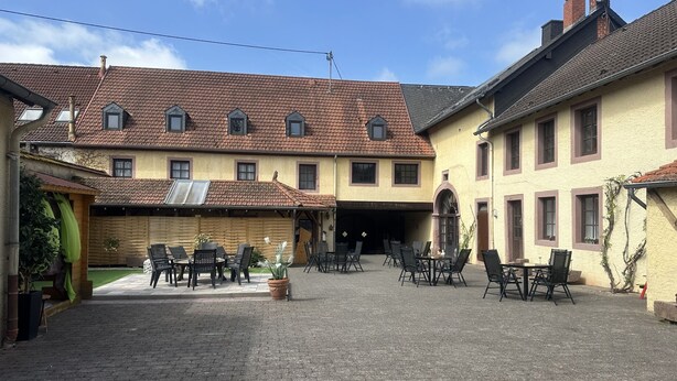 Un patio con mobiliario exterior y un edificio de varios pisos con ventanas y techo de tejas.