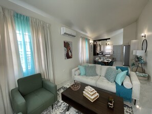 Uma sala de estar moderna com um sofá, uma mesa de centro e uma área de jantar ao fundo.