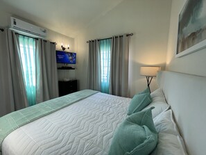 Quarto de hotel com cama, cortinas, televisão na parede e luminária.