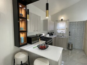 Uma cozinha moderna com bancada branca, fogão, pia e janela com cortinas.