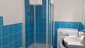 Un baño con ducha, inodoro y lavadora.