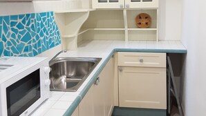Una cocina compacta con armarios blancos, un microondas, un lavamanos y un ventanal pequeño.