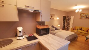 A compact kitchen with a microwave, coffee maker, and tablet on the counter. A bed with a patterned duvet is in the background, and a yellow sofa is visible in the living area. - Hôtel oh sèvres autrement (Sevres)