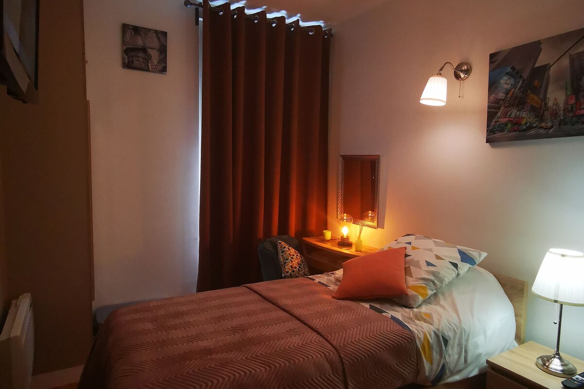 A bedroom with a bed, bedside table, lamp, and a painting on the wall.