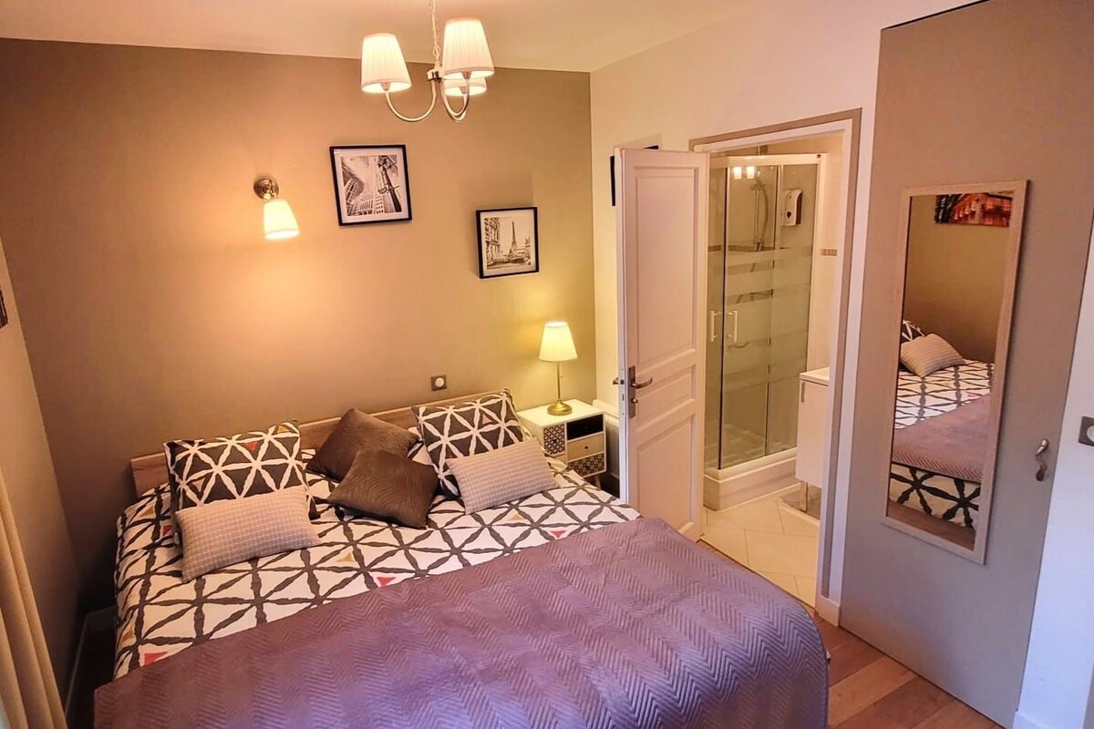 A bedroom with a bed, bedside lamps, a nightstand, a door leading to a bathroom, and a mirror on the wall.