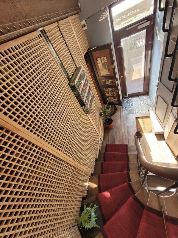 Un escalier recouvert d’une moquette rouge, un mur décoré d’un treillis en bois et une porte portant l’inscription « COUSCOUS-PAELLA ».