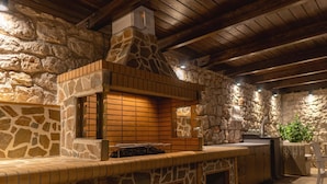 Cocina exterior de piedra y madera con horno de ladrillo, pileta y zona de estar.