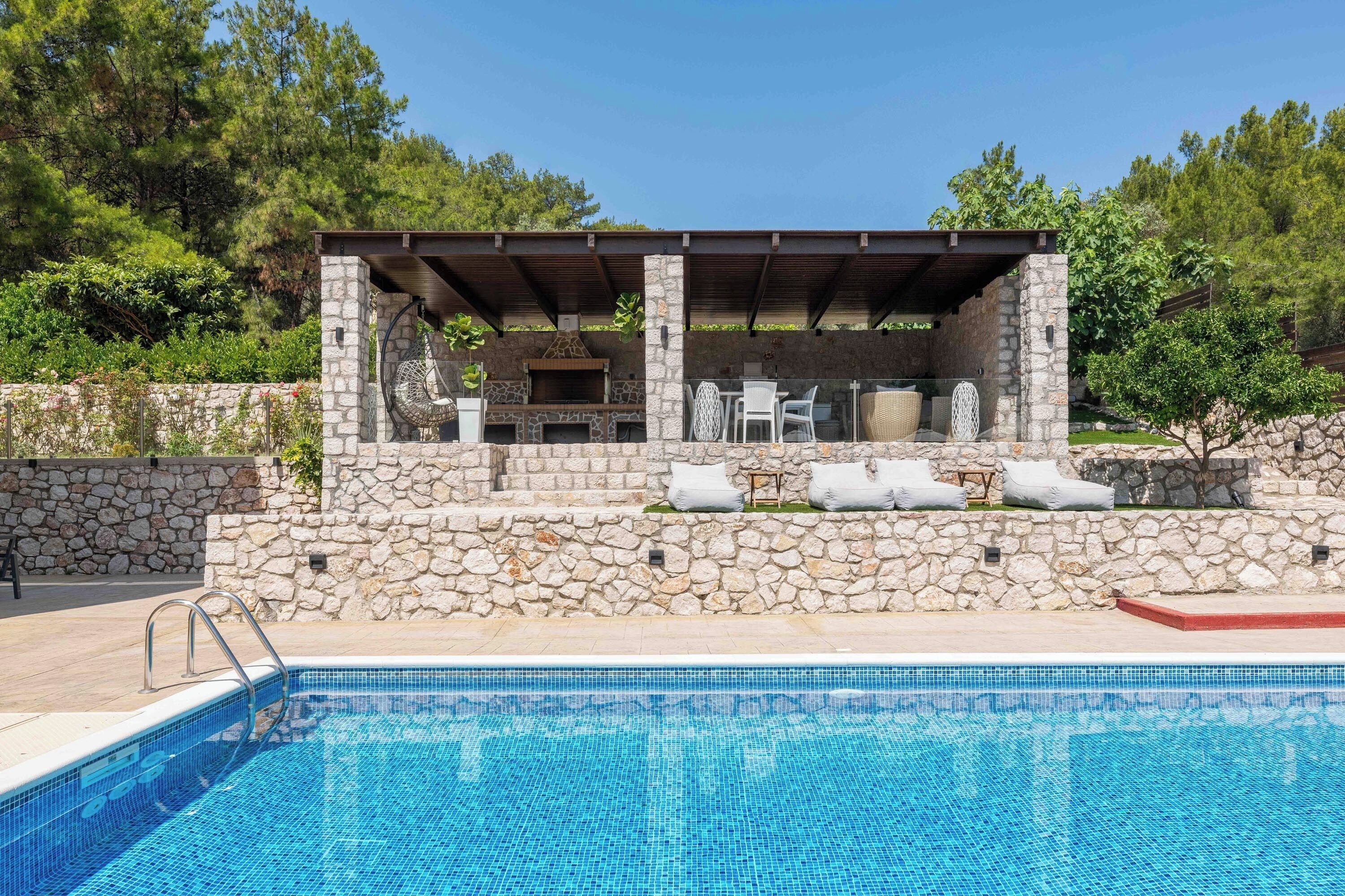 Une piscine avec des murs en pierre et un espace barbecue équipé de mobilier d’extérieur.