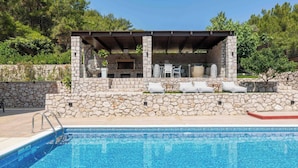 Una piscina con paredes de piedra y zona de barbacoa con mobiliario de exterior.
