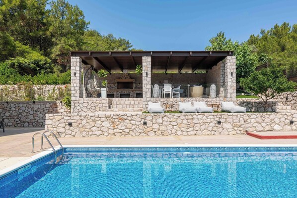 Une piscine avec des murs en pierre et un espace barbecue équipé de mobilier d’extérieur.