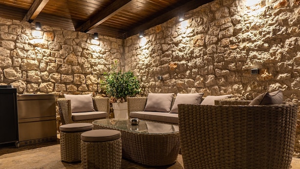 Una habitación con paredes de piedra, muebles de mimbre, una mesa de vidrio y una planta en maceta.